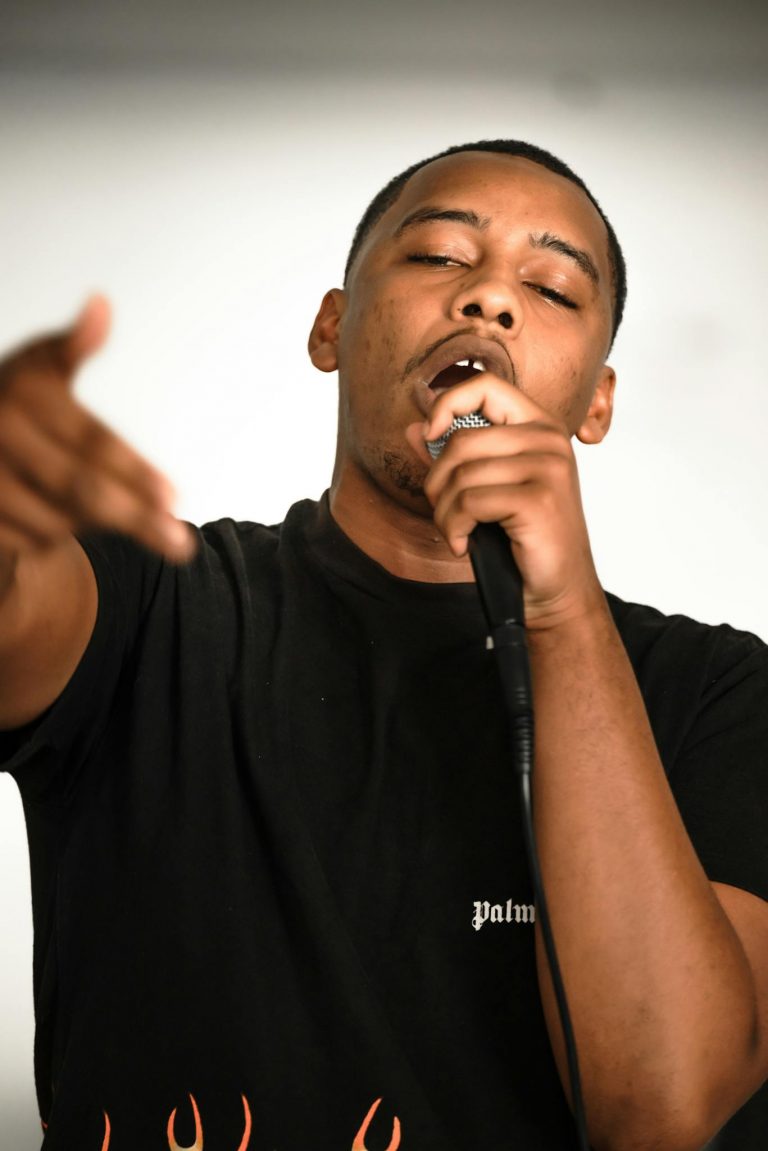Passionate black male rapper in black T-shirt performing with microphone.