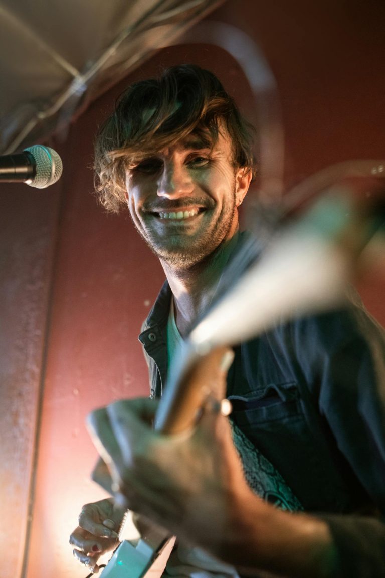 Smiling guitarist performing live with passion and energy on stage.