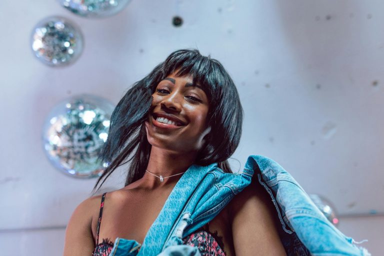 Smiling woman wearing a denim jacket amidst shiny disco balls in an indoor setting.